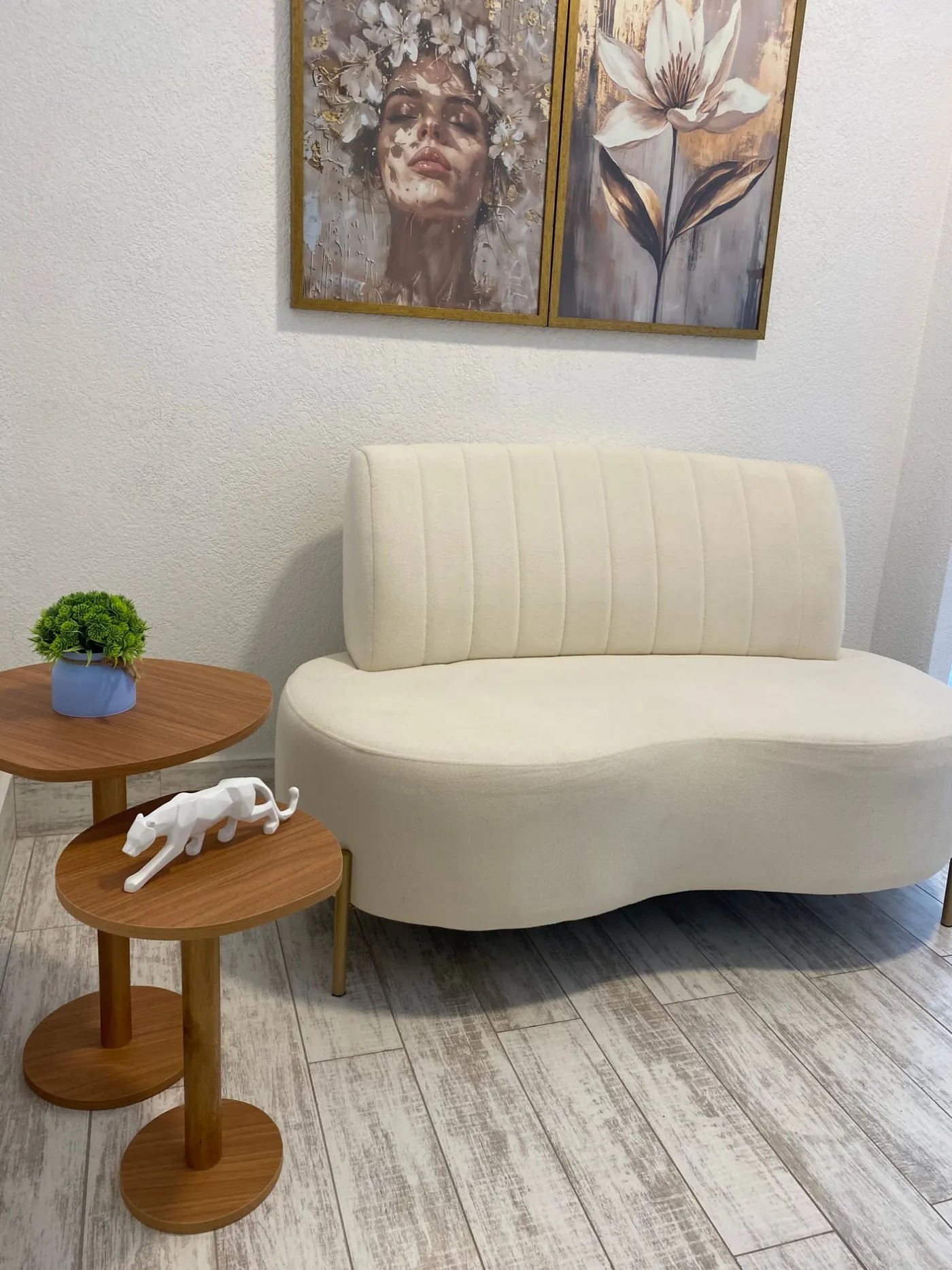 Sala de espera com sofá claro, mesas de madeira e quadros